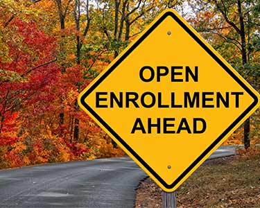 Road surrounded by trees with yellow sign that says Open Enrollment Ahead