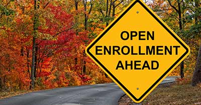 Road surrounded by trees with yellow sign that says Open Enrollment Ahead